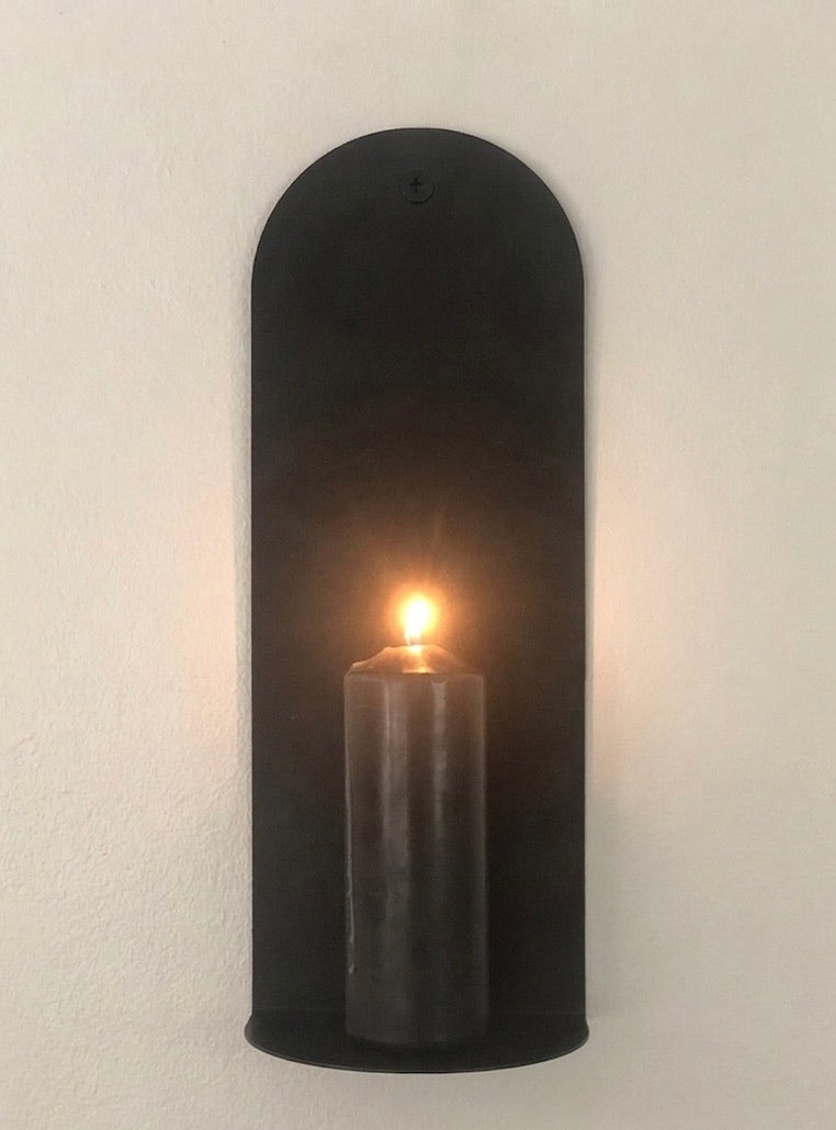 Black wall sconce with a lit candle on a white wall