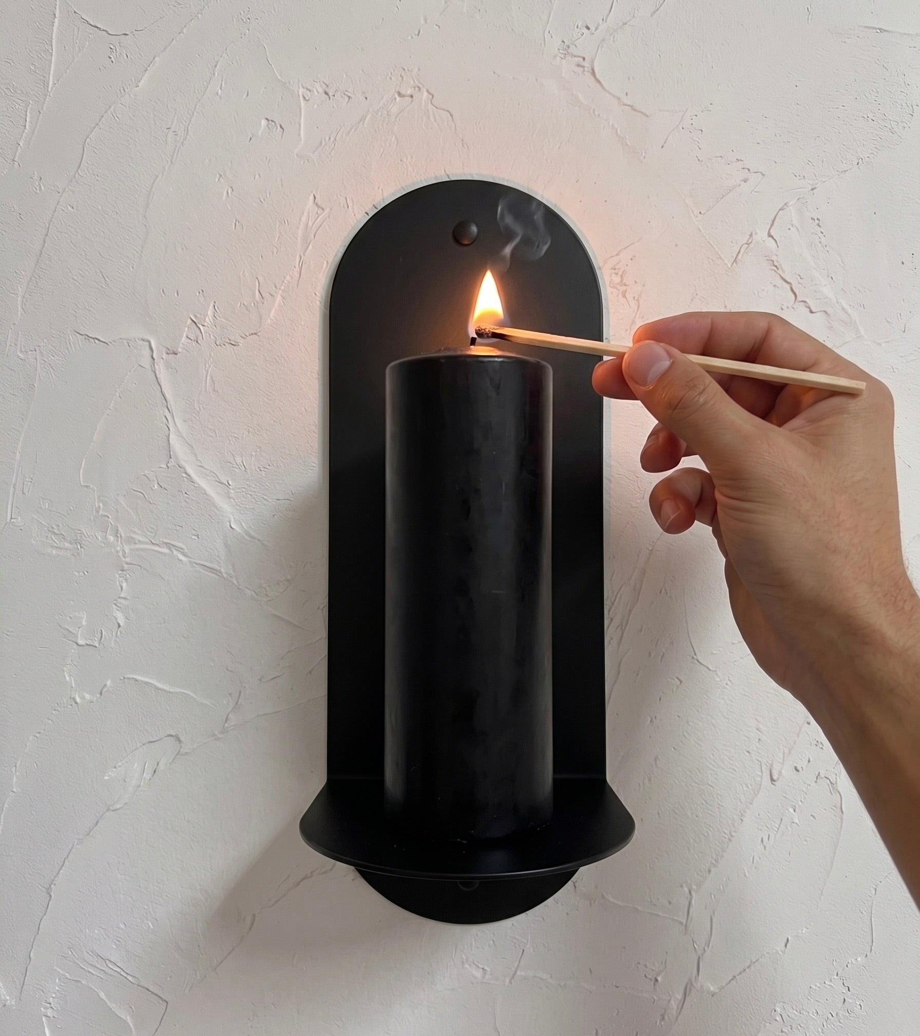 The Oracle wall sconce in Black Ink with illuminated candle on white background, Nomad Studio